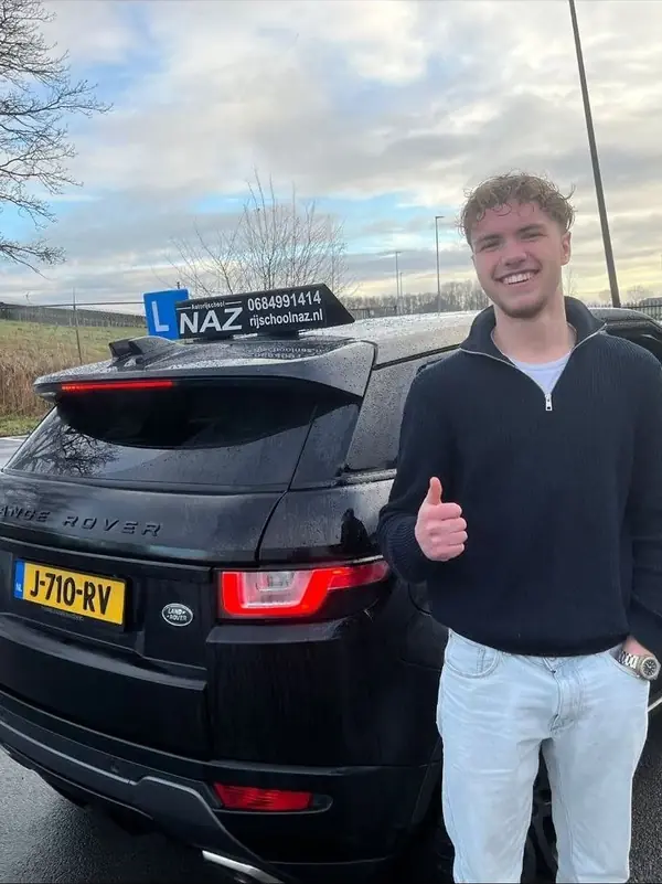 Geslaagde leerling steekt duim op bij de lesauto van NAZ