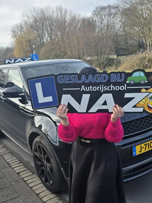 Geslaagde leerling met het bord Geslaagd bij Autorijschool NAZ