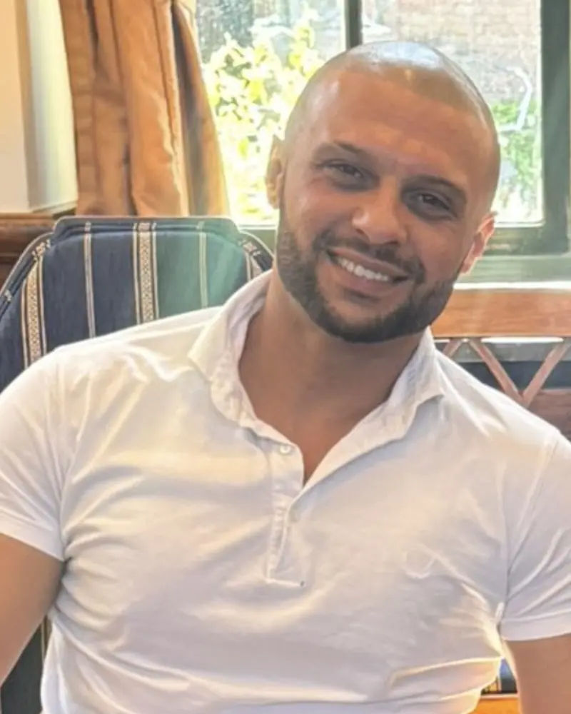 Moayed, instructeur van Autorijschool NAZ, lachend in een wit poloshirt